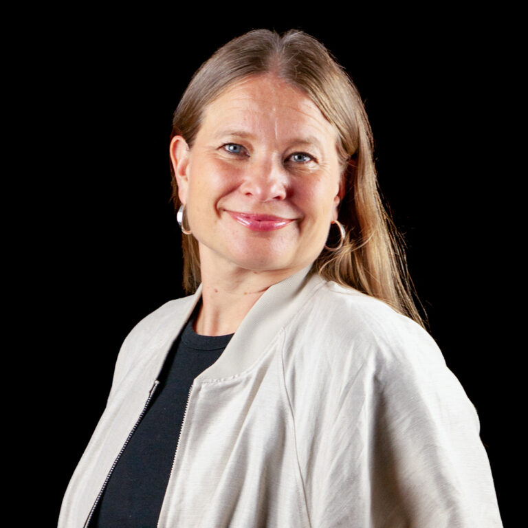 Meskiaikainen nainen, jolla on olkapäille ulottuvat hiukset, hymyilee mustalla taustalla.